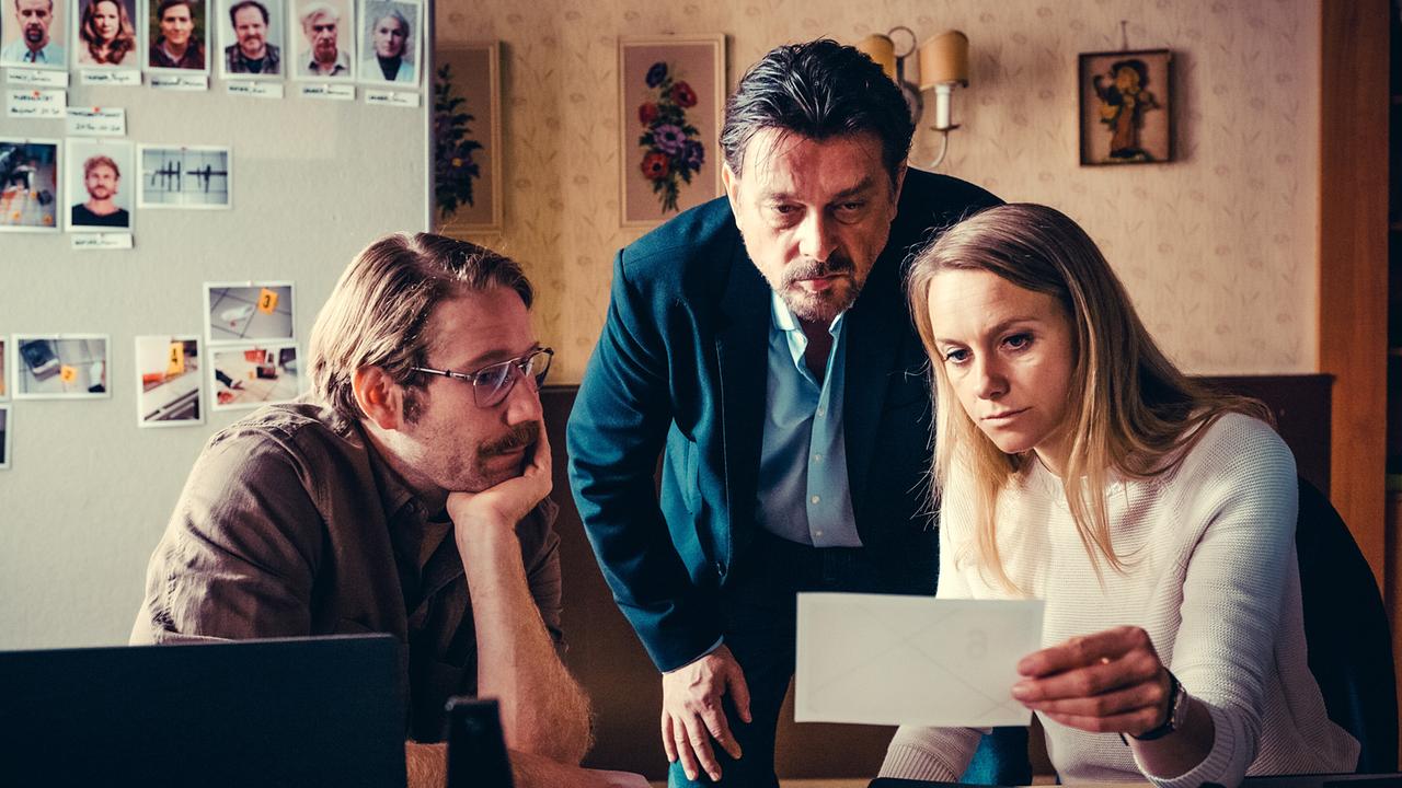 Bernd Kofler, Sascha Bergmann und Anni Sulmtaler analysieren gemeinsam Unterlagen und Fotos in einem Ermittlungsraum.