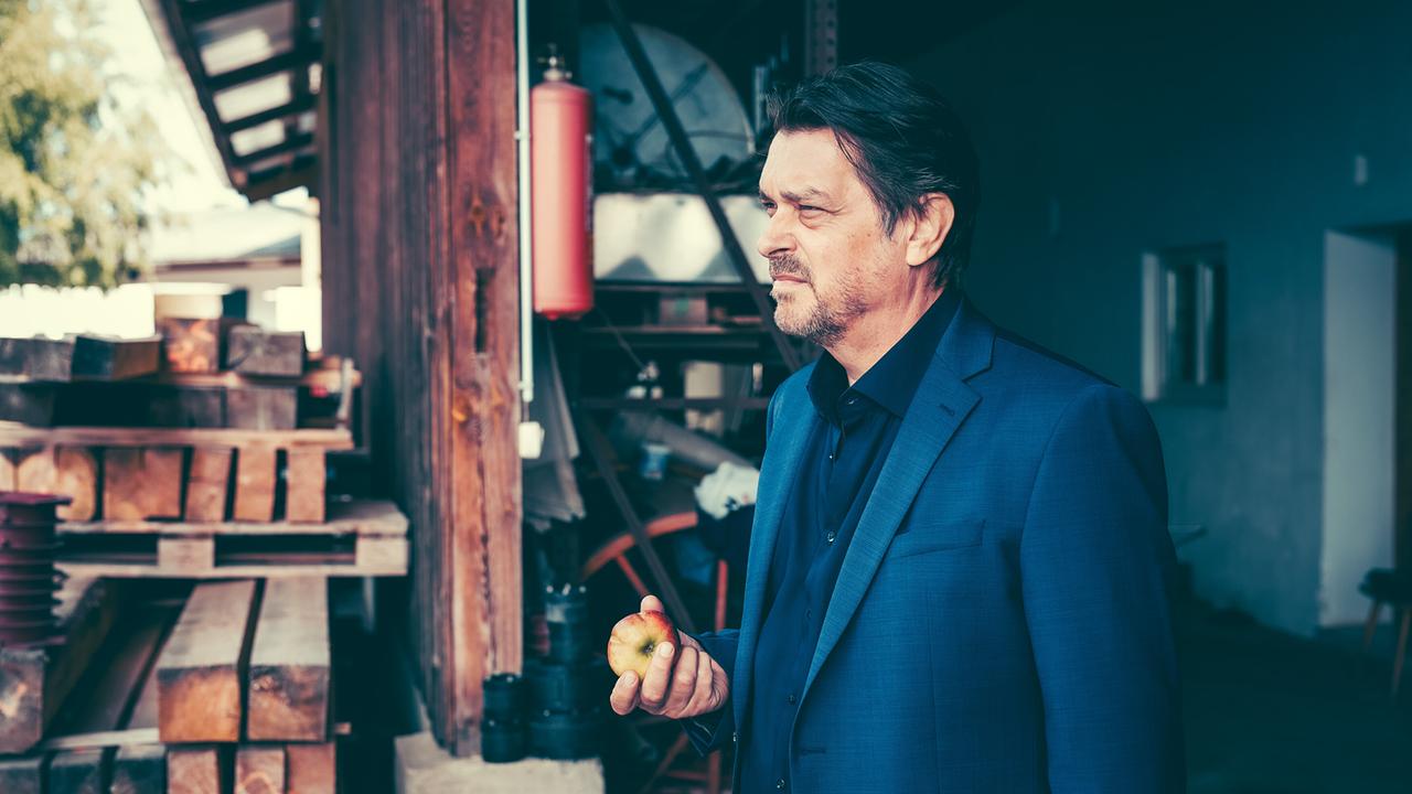 Hary Prinz im blauen Sakko steht vor einem Holzlager und hält einen Apfel.