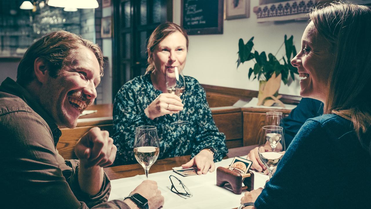 Christoph Kohlbacher, Bettina Mittendorfer und Anna Unterberger sitzen lächelnd mit Weingläsern an einem Tisch in einem Gastraum.
