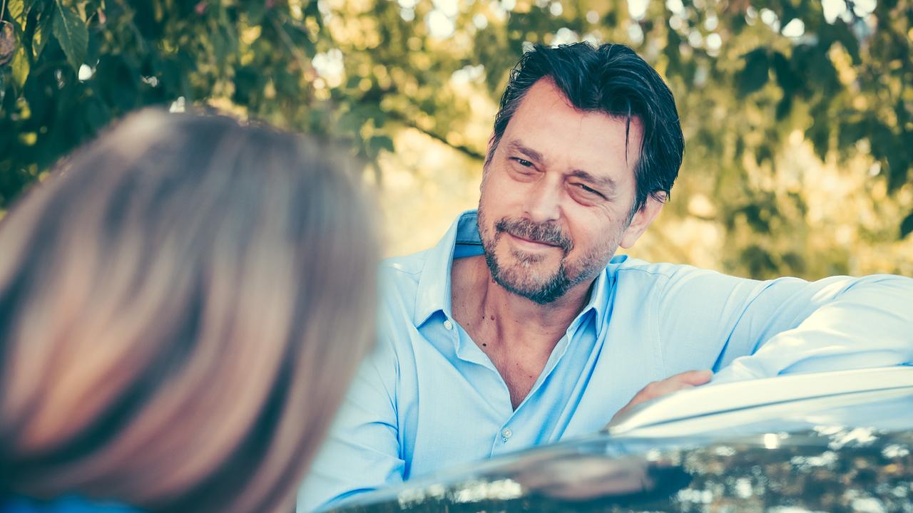 Hary Prinz lehnt im Grünen an einem Auto und lächelt Anna Unterberger an.