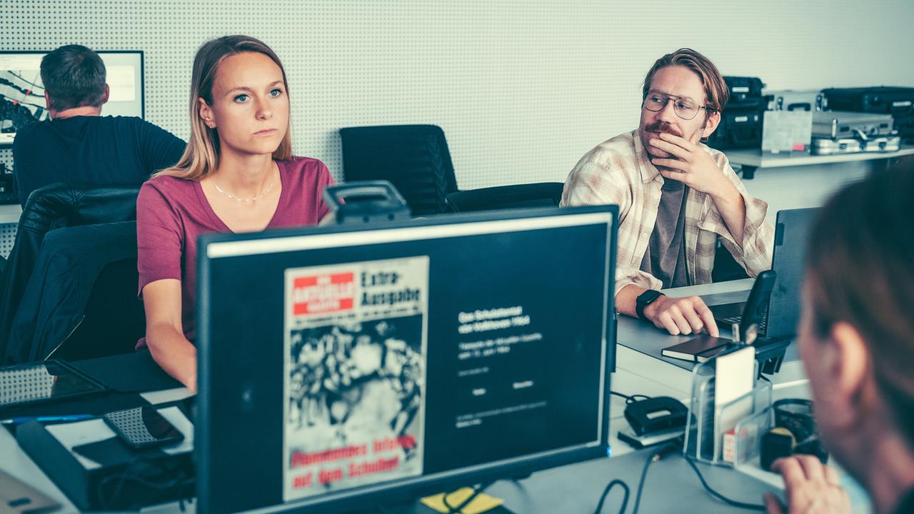 Anna Unterberger, Christoph Kohlbacher und weitere Menschen sitzen im Büro vor Computern, auf einem Bildschirm ist eine Zeitungsseite zu sehen.