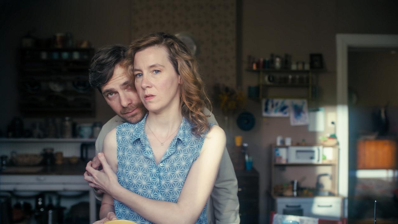 © ORF/MR Film Stefan Pohl umarmt Franziska Hackl in einem blauen gemusterten ärmellosen Hemd in einer Küche.