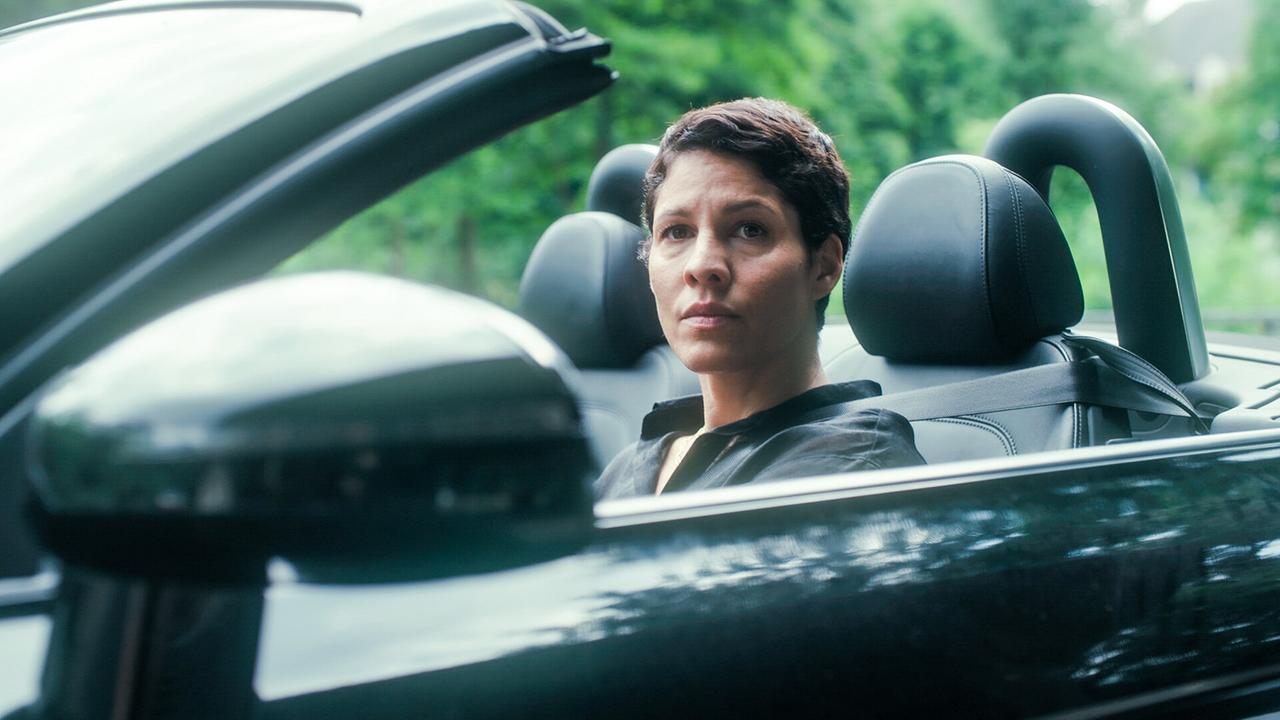 © ORF/MR Film Jasmin Gerat sitzt in einem schwarzen Cabrio und schaut ernst nach vorne.