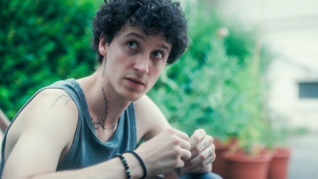 Etienne Halsdorf, im Tanktop und mit sichtbaren Tattoos, sitzt im Freien und scheint nachdenklich.