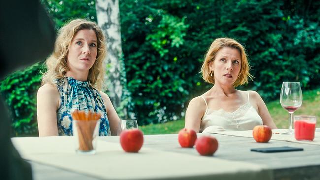 Franziska Hackl und Franziska Weisz sitzen im Freien an einem Gartentisch mit Getränken, roten Äpfeln und Snacks, im Hintergrund Bäume und Grün.