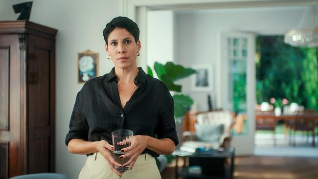 © ORF/MR Film Jasmin Gerat steht in einem hellen Wohnzimmer und hält ein Glas, im Hintergrund ist eine Terrasse mit Gartenmöbeln sichtbar.