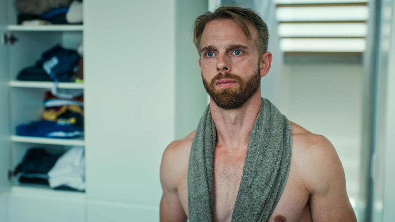 Mads Hjulmand mit nacktem Oberkörper und einem Handtuch um den Hals steht in einem Ankleidebereich mit offenem Schrank.