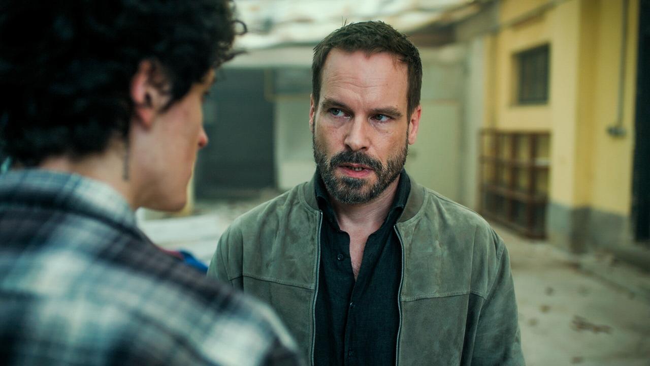  Etienne Halsdorf und Wanja Mues stehen sich an einem halboffenen, etwas heruntergekommenen Ort gegenüber.