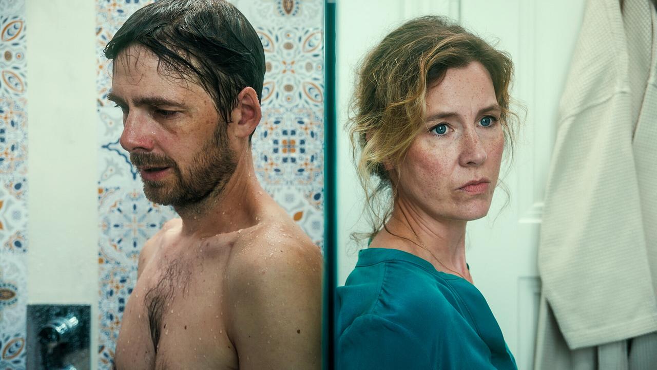 Stefan Pohl nackt unter der Dusche lehnt an der Duschwand Rücken an Rücken mit Franziska Hackl, die außen an der Duschwand lehnt