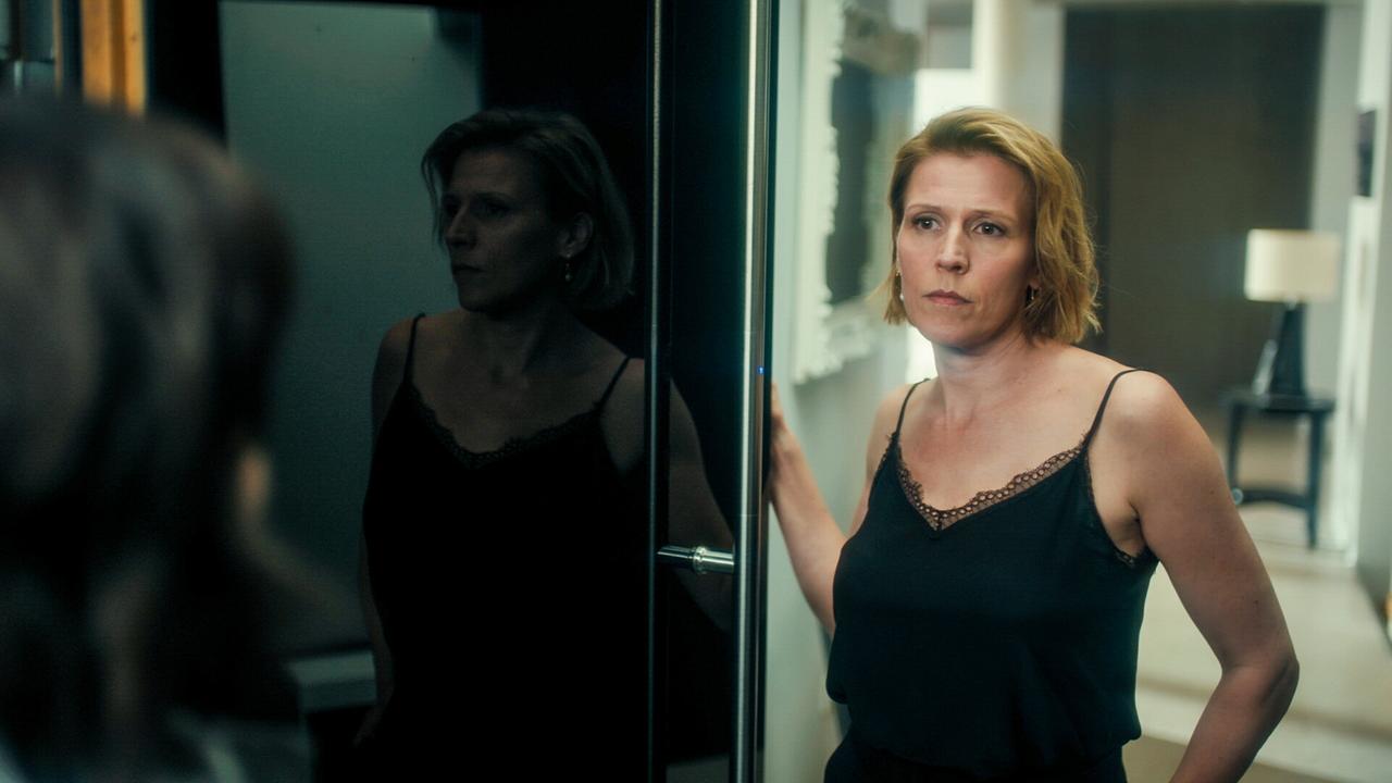  Franziska Weisz in einem  schwarzes Oberteil mit Spaghetti-Trägern in einem modernen Raum lehnt an einer schwarzen Hochglanz-Schiebetür.