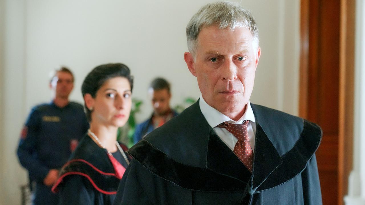 © ORF/MR Film/Petro Domenigg Zeynep Buyraç und Andreas Lust in schwarzen Richterroben stehen in einem hellen Raum, im Hintergrund sind Polizisten zu sehen.