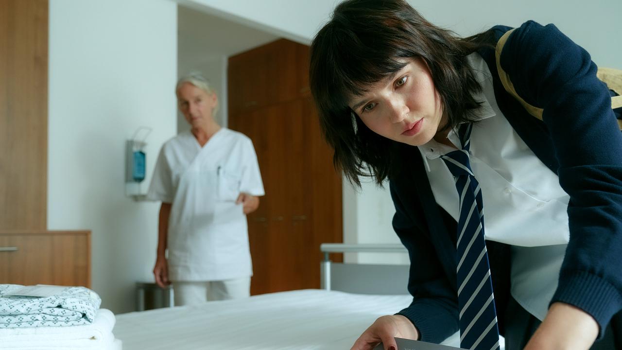 © ORF/MR Film/Petro Domenigg Paulina Hobratschk in Schuluniform beugt sich über eine Schublade im Krankenhauszimmer, während im Hintergrund eine Krankenschwester steht.