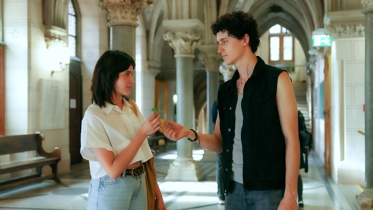 © ORF/MR Film/Petro Domenigg Etienne Halsdorf überreicht Paulina Hobratschk ein vierblättriges Kleeblatt am Gang eines historischen Gebäudes.