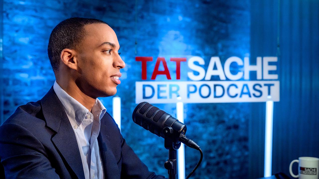 © ORF/Hans Leitner Stefan Legnlinger im Studio vor blauem Hintergrund mit Aufschrift 'TATsache – Der Podcast'