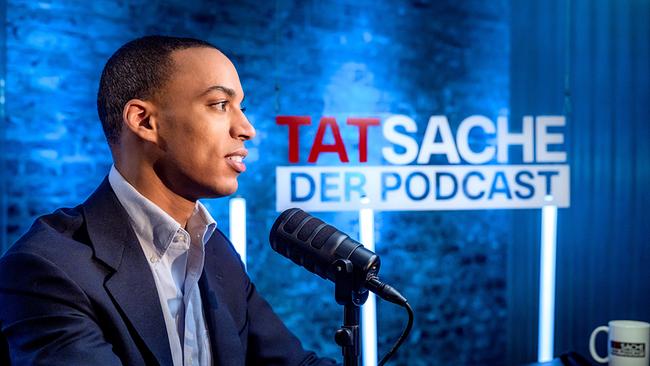 Stefan Legnlinger im Studio vor blauem Hintergrund mit Aufschrift 'TATsache – Der Podcast'