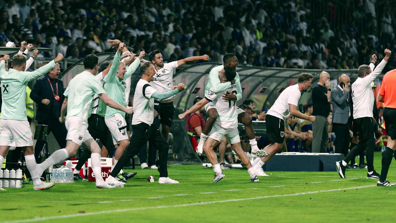 Spieler und Betreuer jubeln ausgelassen an der Seitenlinie eines voll besetzten Stadions über den wichtigen Auswärtssieg gegen Bosnien und Herzegowina.