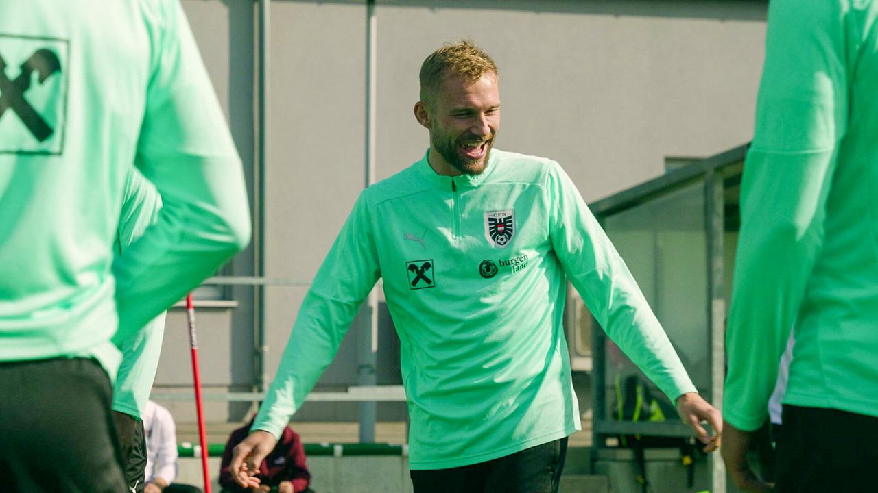 Konrad Laimer bewegt sich lachend im grünen Trainingsoutfit auf einem Trainingsplatz.