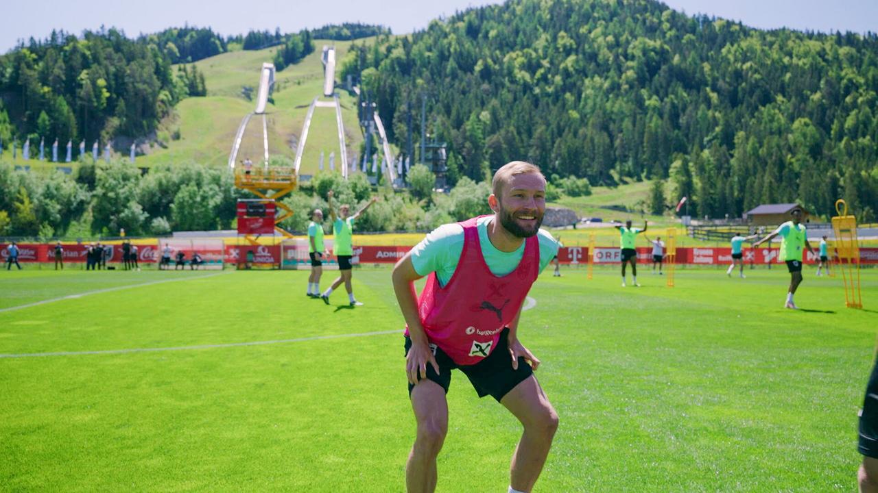 Konrad Laimer beim Training bei Sonnenschein auf einem grünen Trainingsplatz in alpiner Umgebung.