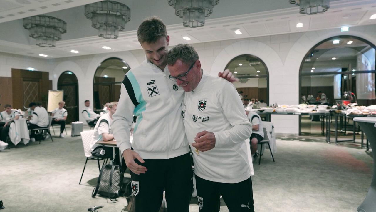 Stefan Posch und Teamchef Ralf Rangnick stehen eng beieinander in einem großen Speisesaal, im Hintergrund weitere Teamspieler an den Tischen.