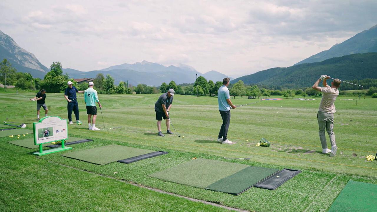 Eine Gruppe von Spielern trainiert auf einer Driving Range mit Blick auf eine bergige Landschaft.