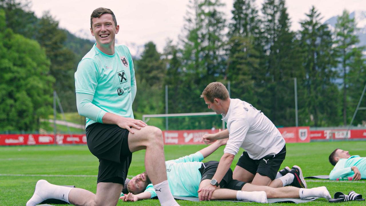 Michael Gregoritsch und weitere Spieler absolvieren Dehnübungen auf dem Rasen eines Trainingsplatzes im Freien unter Anleitung.