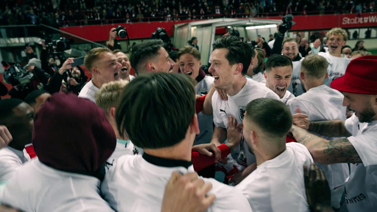 Spieler feiern dicht gedrängt auf dem Spielfeld, umgeben von Medien und Fans.