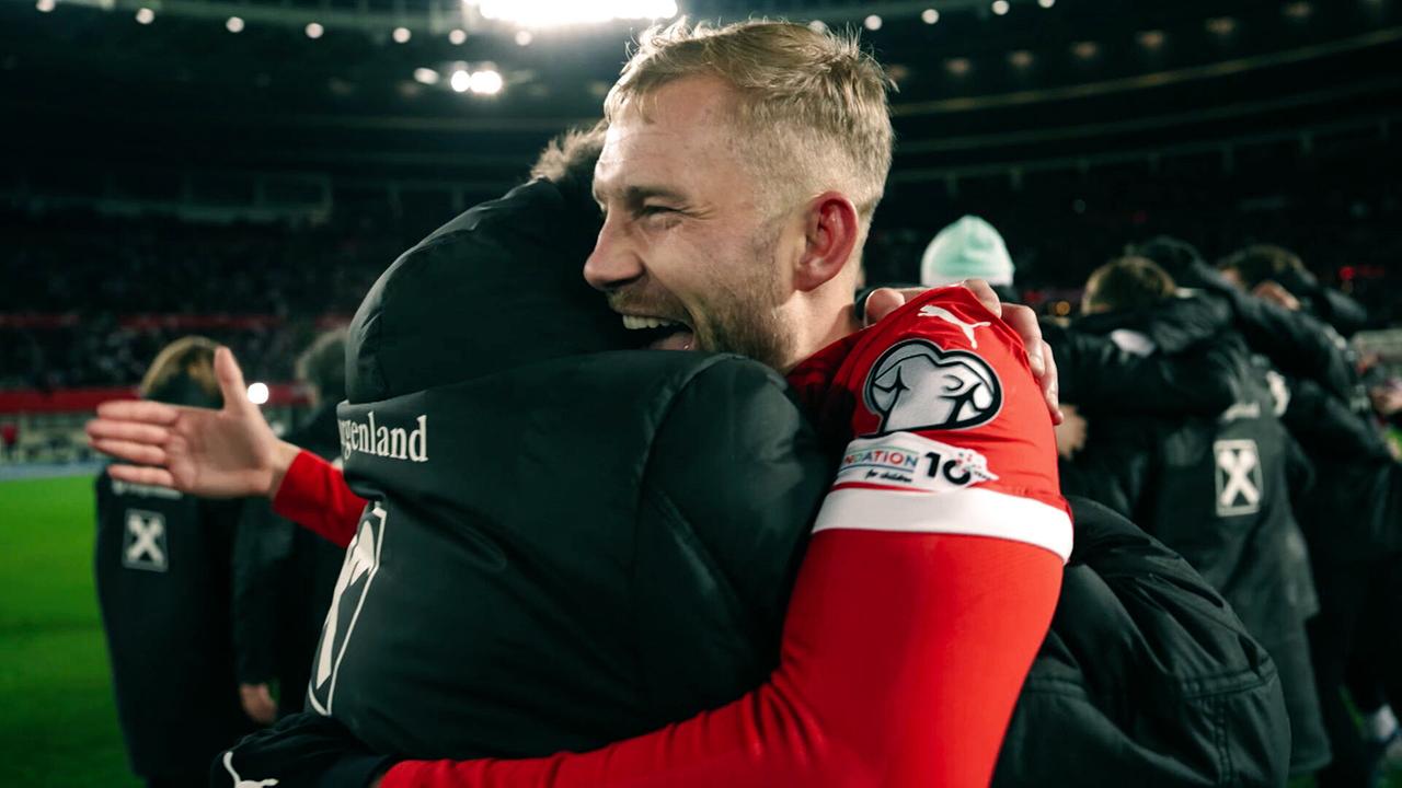 Zwei Teammitglieder im Vordergrund umarmen sich vor Freude und Erleichterung im Stadion, dahinter weitere Teammitglieder.