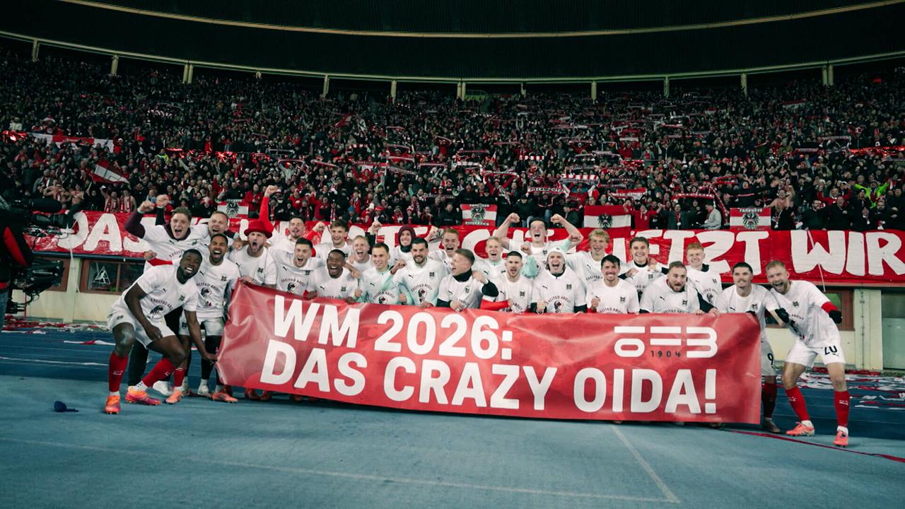 Das ÖFB-Team posiert im Stadion mit einem Banner „WM 2026: Das crazy Oida“ vor jubelnden Fans.