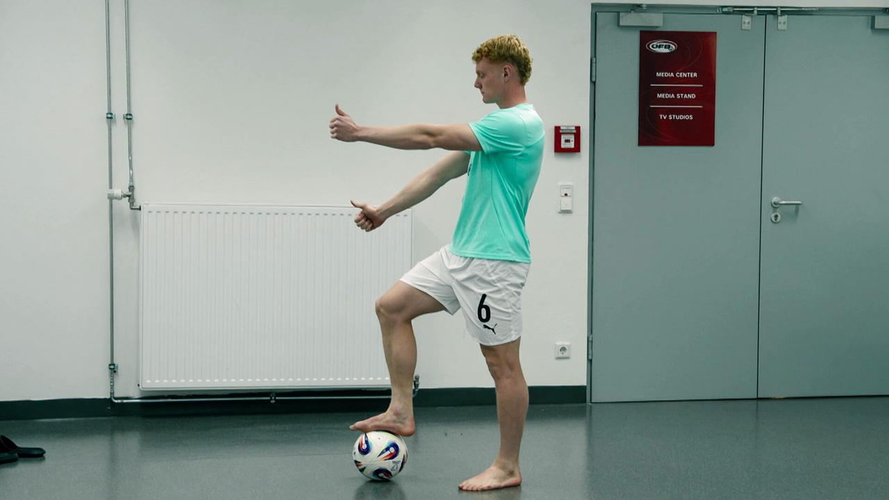 Nicolas Seiwald balanciert barfuß auf einem Fußball in einem Innenraum und trainiert seine Koordination in einem Innenraum.