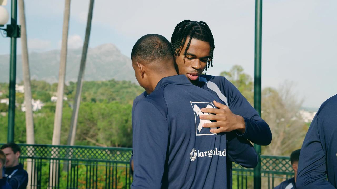 David Alaba und Carney Chukwuemeka im Teamtrainingslager umarmen sich freundschaftlich auf einer Terrasse in Marbella.
