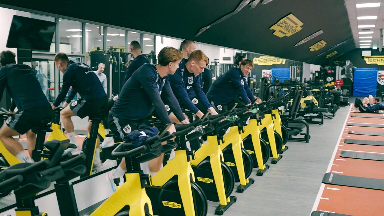 Mehrere Sportler trainieren in einem Fitnessraum auf gelben Indoor‑Fahrrädern im neu gebauten ÖFB-Campus in der Seestadt.