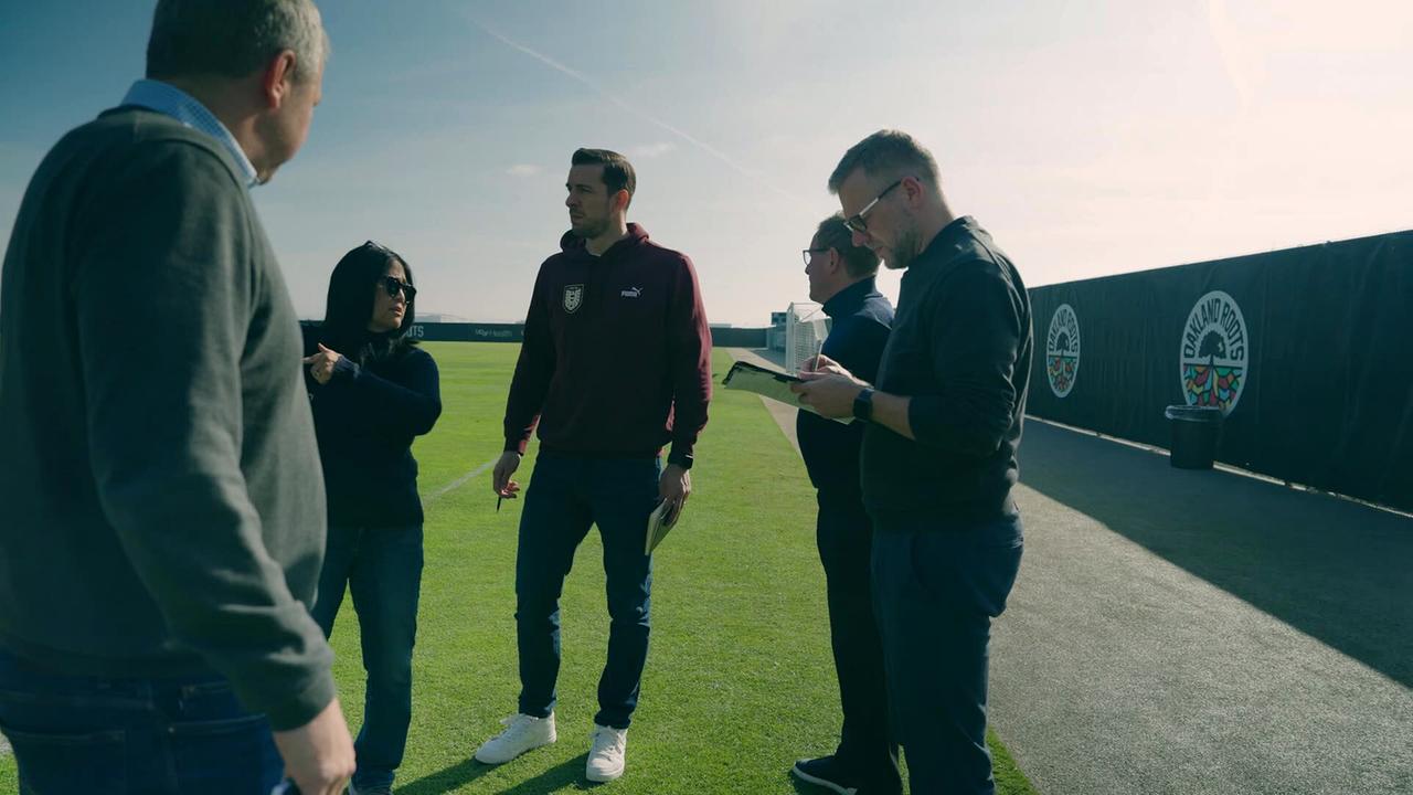 Die Teammanager Mario Margreiter und Lennart Coerdt stehen mit Teamchef Ralf Rangnick am Rand eines Fußballplatzes und sind auf der Suche nach einem geeigneten Camp während der Weltmeisterschaft.