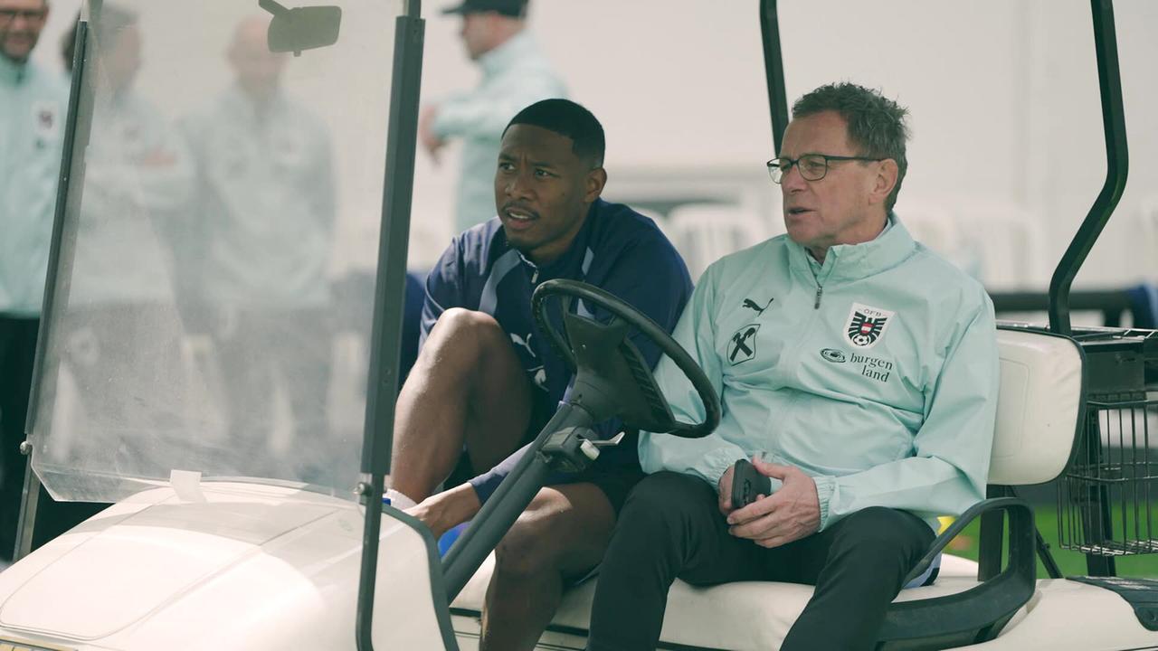 David Alaba und Teamchef Ralf Rangnick sitzen in einem Golfcart auf einem Trainingsgelände und unterhalten sich. 
