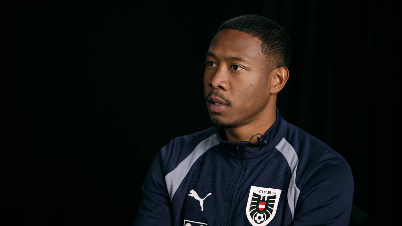David Alaba in Sportkleidung wird in einem Studio‑Setting vor schwarzem Hintergrund interviewt.