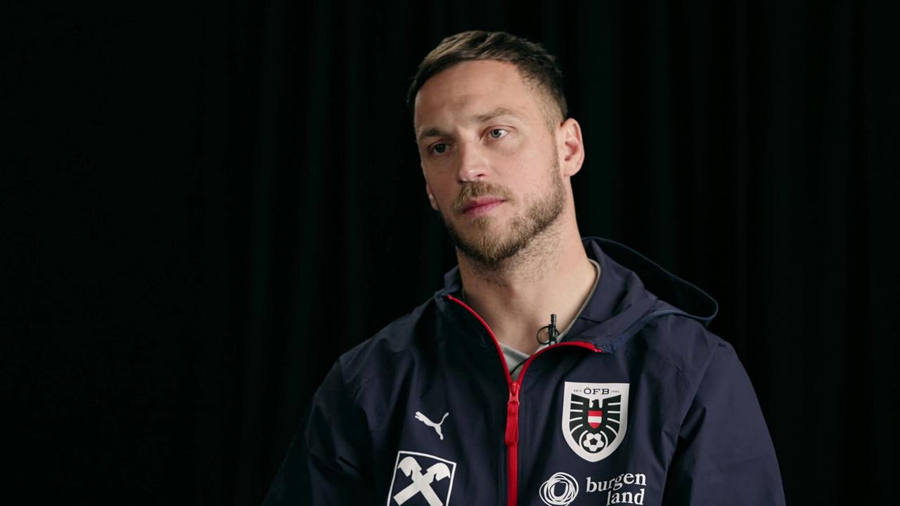 Marko Arnautović in Sportkleidung wird in einem Studio‑Setting vor schwarzem Hintergrund interviewt.