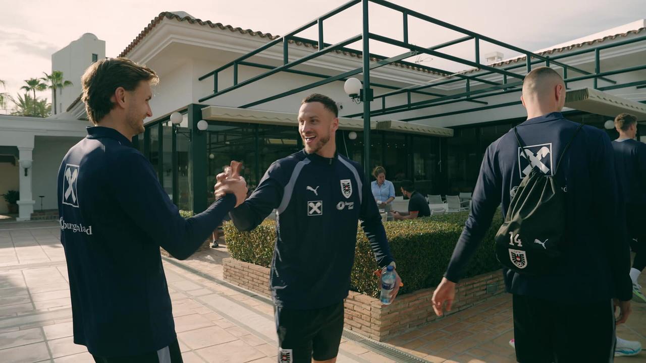 Stefan Posch und Marko Arnautović geben sich im Freien vor einem Gebäude im Teamcamp in Marbella einen Handschlag, während andere vorbeigehen.