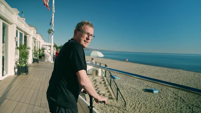 Teamchef Ralf Rangnick lehnt auf einer Strandpromenade in Santa Barbara am Geländer und blickt aufs Meer.