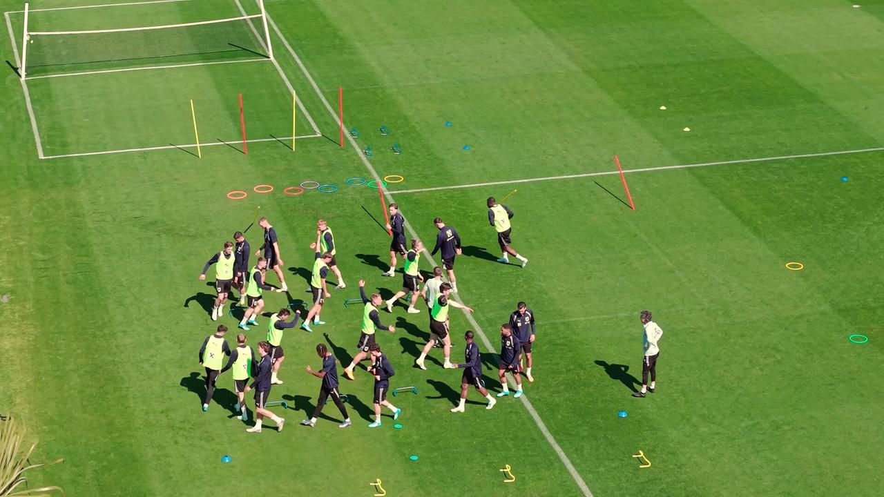 Mehrere Spieler machen Koordinationsübungen mit kleinen Hürden auf dem Rasen beim Trainingscamp in Marbella.