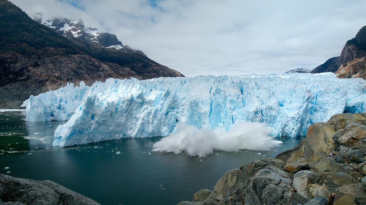 Die eisblaue Wand eines Gletschers, ein Teil der Eisfront ist abgebrochen und fällt gerade ins Wasser