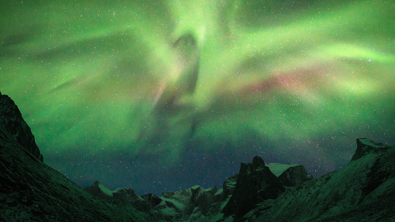 Grüne und rote Nordlichter über einer Berglandschaft in Alaska