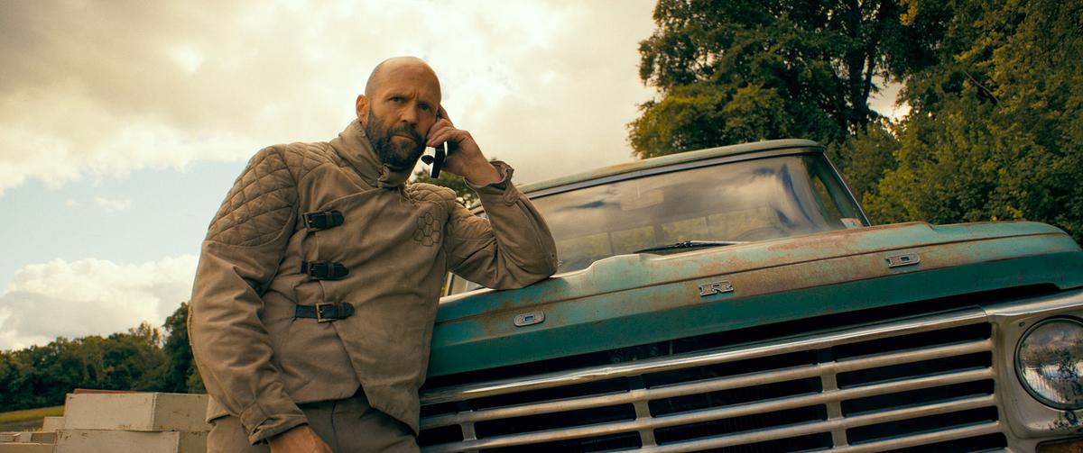 © ORF/LEONINE Studios/Amazon MGM Studios Jason Statham als Adam Clay in dem Schutzanzug eines Imkers lehnt er sich an der Motorhaube eines türkisfarbenen, rostigen Pick-Up und telefoniert mit seinem Handy