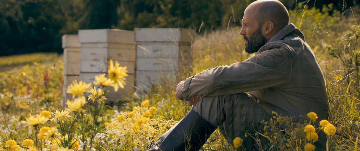 © ORF/LEONINE Studios/Amazon MGM Studios Jason Statham sitzt als Adam Clay in der Schutzbekleidung eines Imkers in einer gelb blühenden Wiese, im Hintergrund sind Bienenstöcke zu sehen