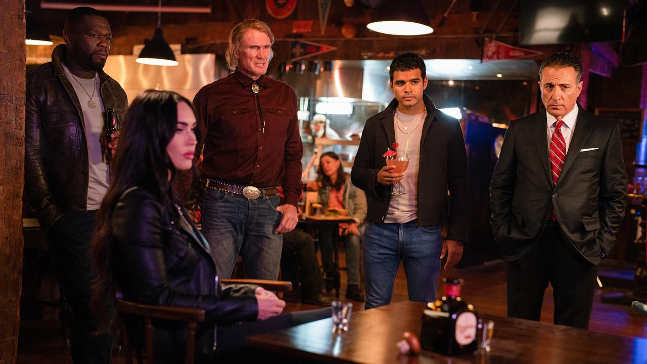 In einem Gasthaus sitzt eine Frau an einem Tisch, hinter ihr stehen vier Männer - alle fünf blicken in dieselbe Richtung