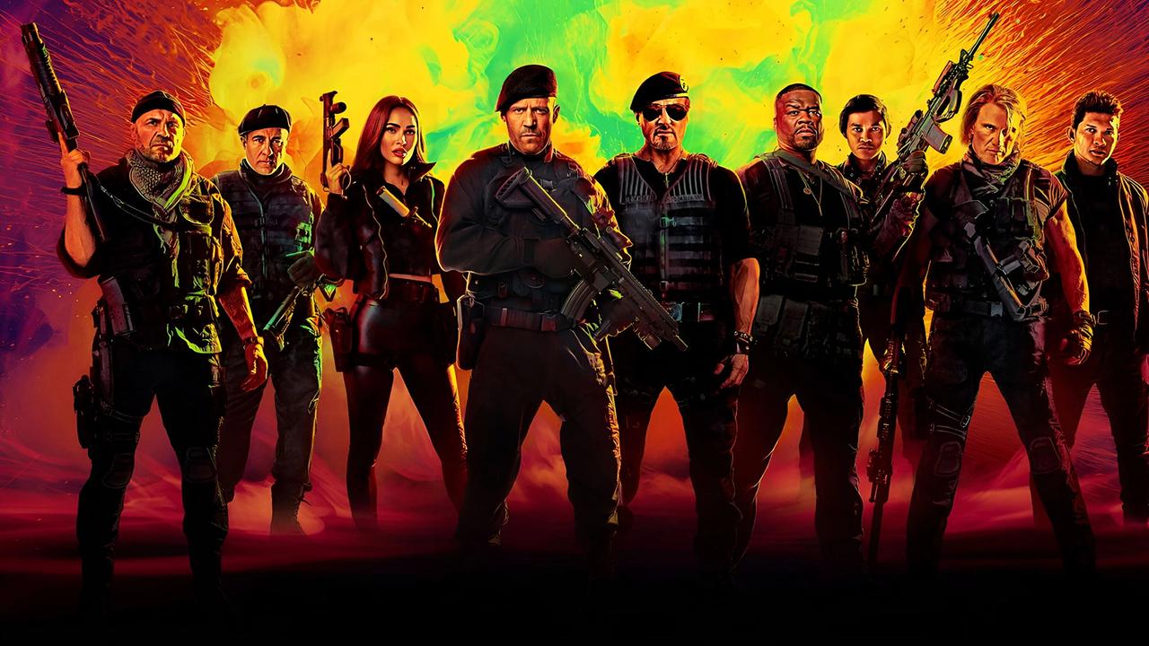 Acht Männer und eine Frau - alle tragen Kampfausrüstung, einige sind bewaffnet - alle stehen vor einem rot-gelb-grünen Hintergrund