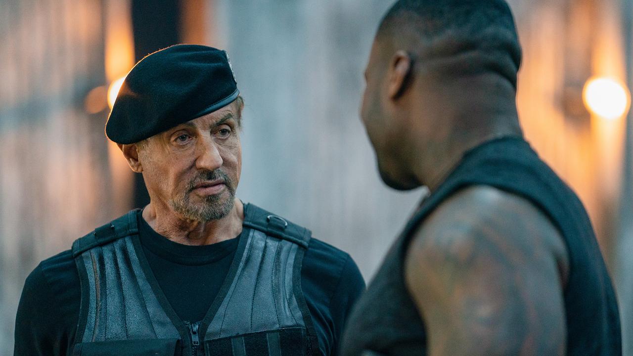 Ein schwarz bekleideter Mann mit Schutzweste und Barett unterhält sich mit einem tätowierten Mann, der ihm gegenübersteht