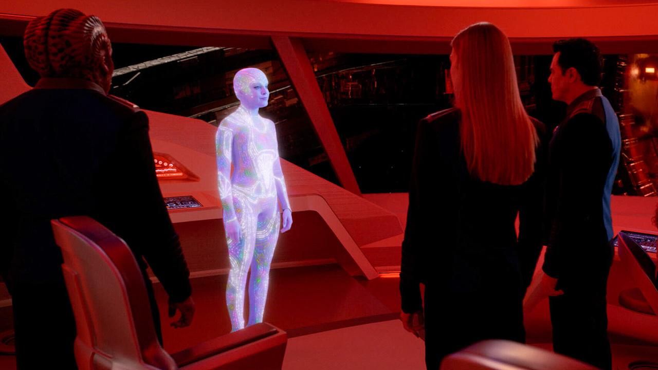 Die Kommando-Brücke der Orville ist rot beleuchtet - die Crew steht verwundert vor einer Person, die hell zu leuchten scheint und einen hautengen, gemusterten Anzug trägt