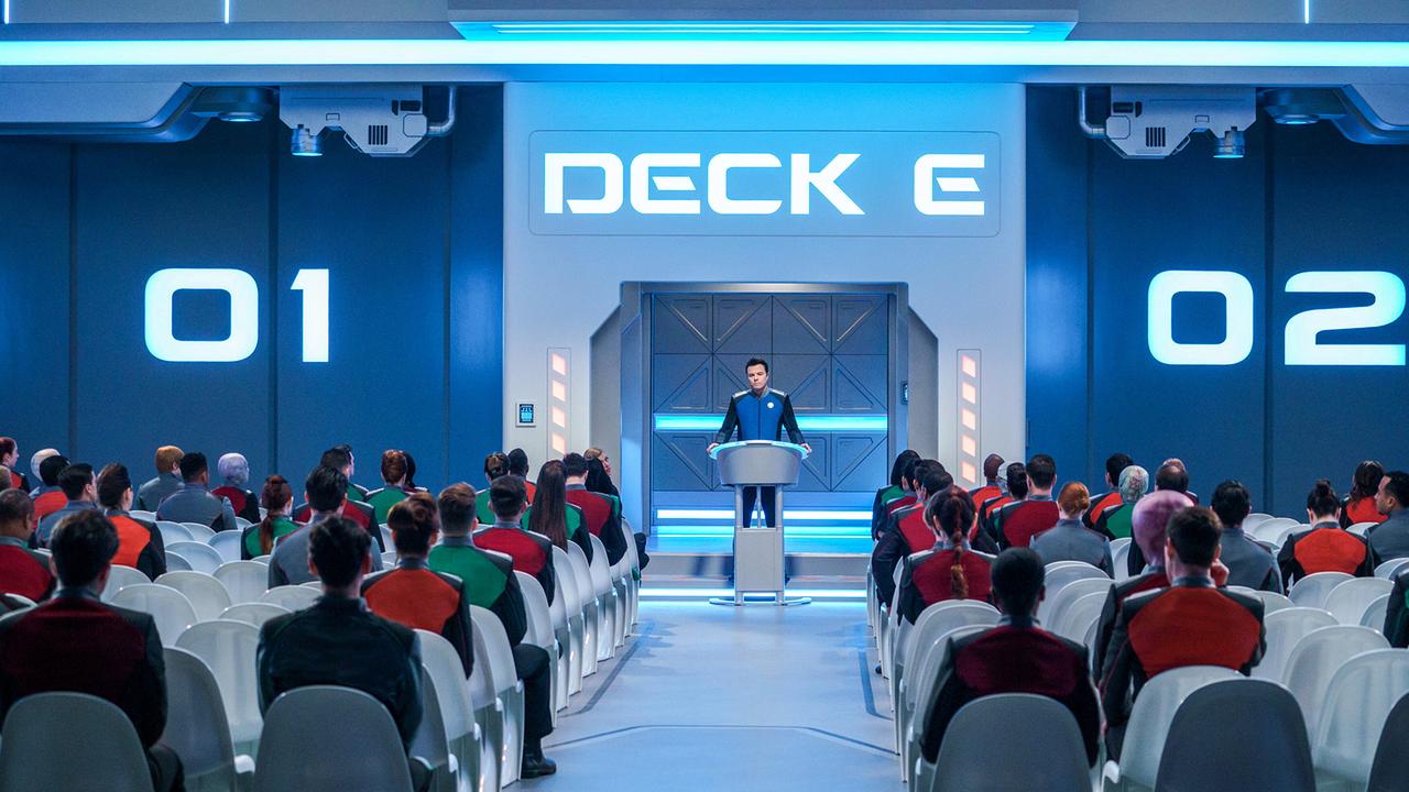 Seth MacFarlane als Captain Ed Mercer, er steht am Rednerpult einer großen Halle, im Publikum sitzen Crewmitglieder der Orville