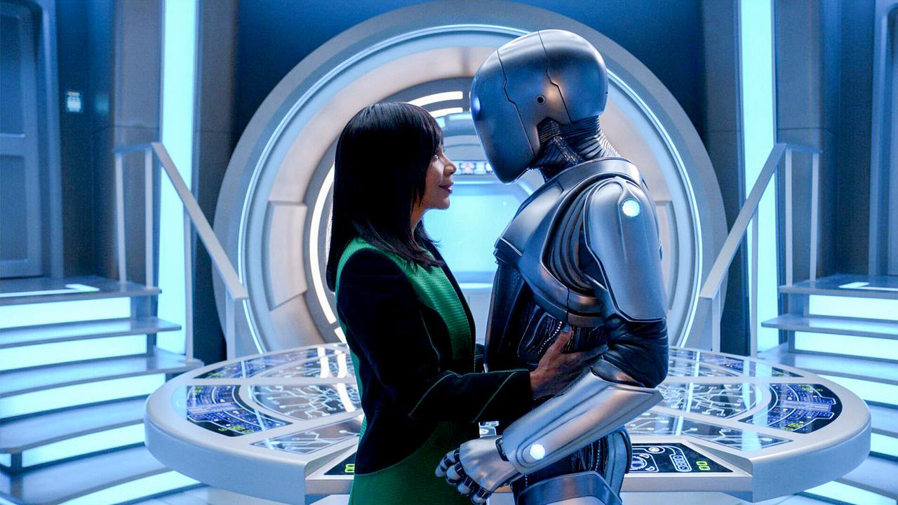 © ORF/ProSieben/20th Century Studios/Hulu/Gilles Mingasson In einem futuristischen hellblau leuchtenden Ambiente stehen eine Frau in grün-schwarzer Uniform und ein silberfarbender Android gegenüber, umarmen sich und blicken sich tief in die Augen