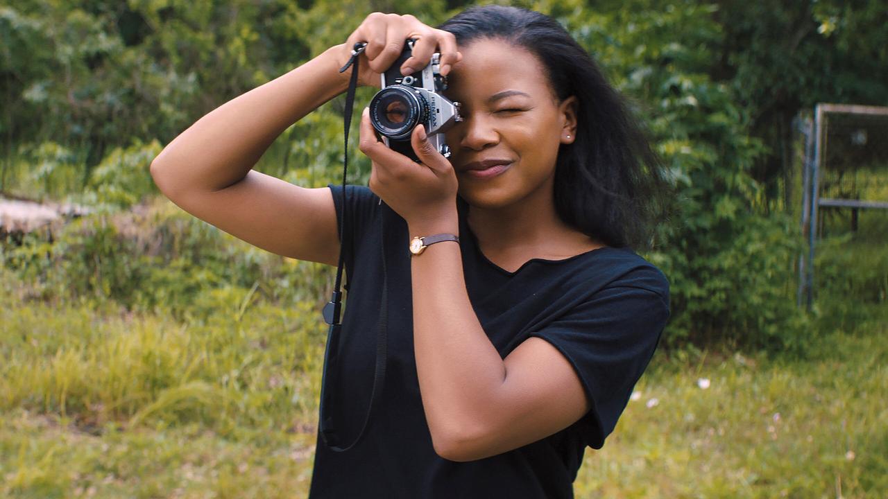 Christina Eames im schwarzen T-Shirt, steht auf einem bewaldeten Wiesenstück und fotografiert mit einer Spiegelreflexkamera 