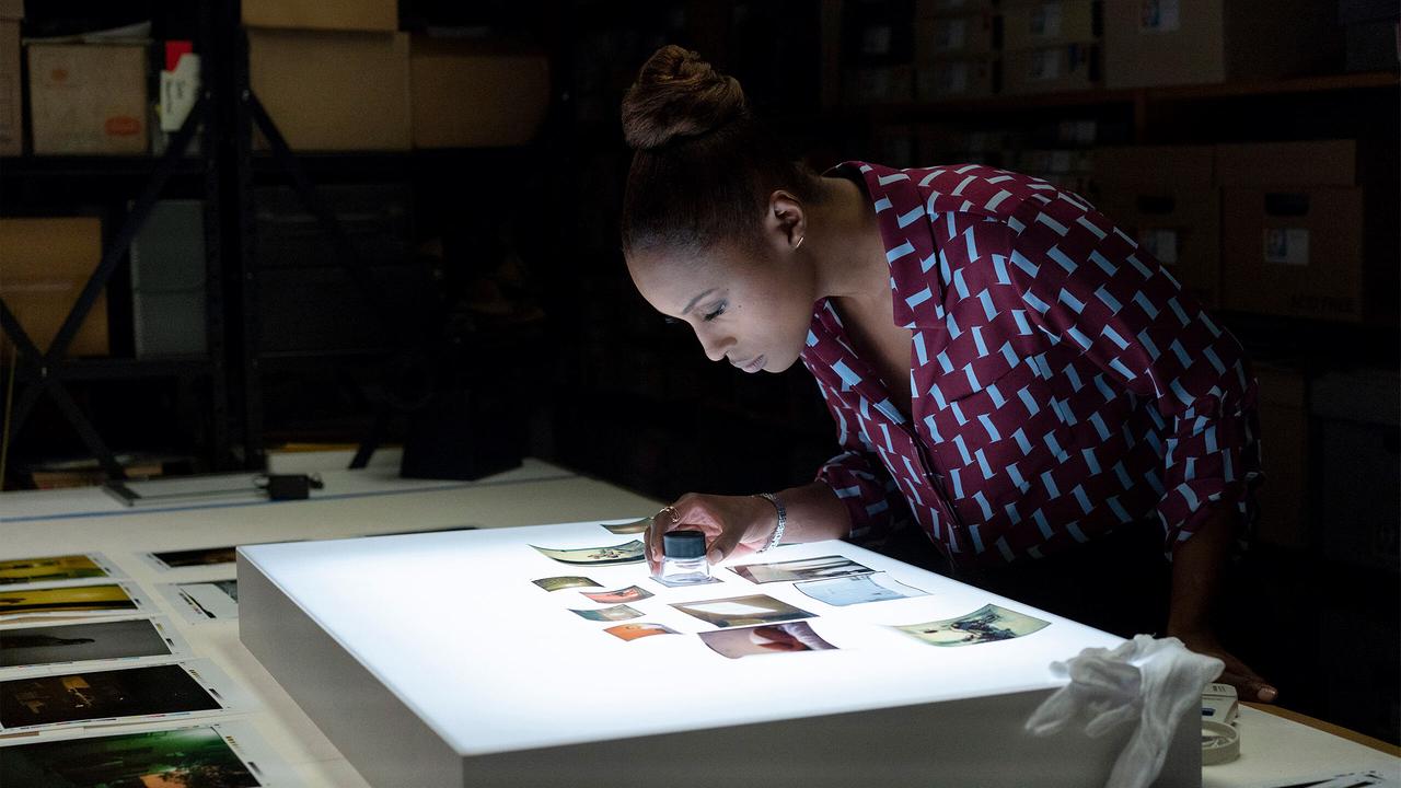 Mae steht an einem Lichttisch und sieht sich mit einer Lupe Fotoaufnahmen an